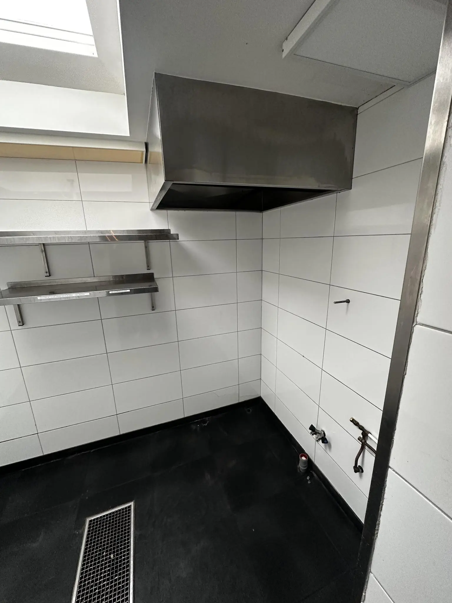 Wit betegelde horecakeuken in aanbouw met afzuigkap, wandrekken en leidingaansluitingen op het Sint-Agathaplein.